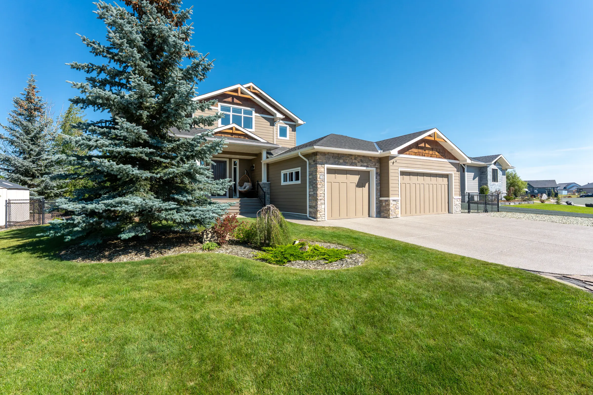 8 Monterra Cove seen from the street: a Craftsman-gabled executive home with stone detailing, mature spruce, and a wide concrete drive.