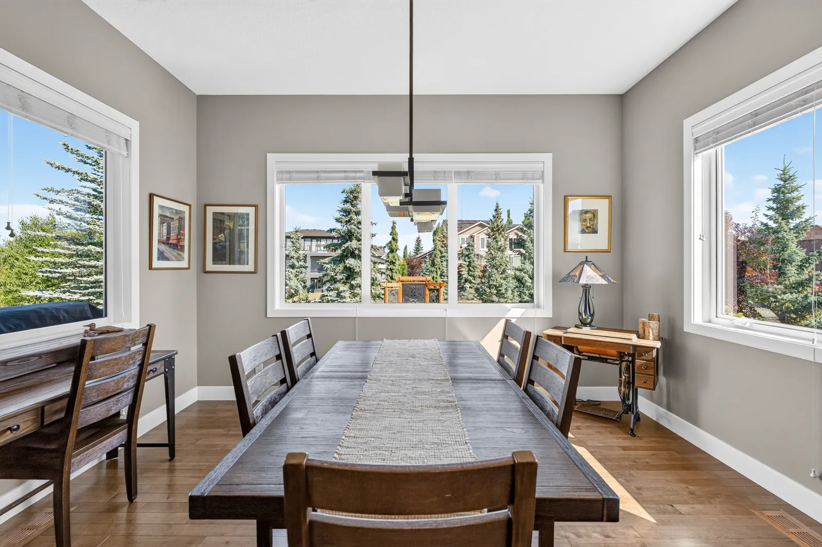 The dining room at 8 Monterra Cove, wrapped in windows onto mature spruce, with maple hardwood underfoot.